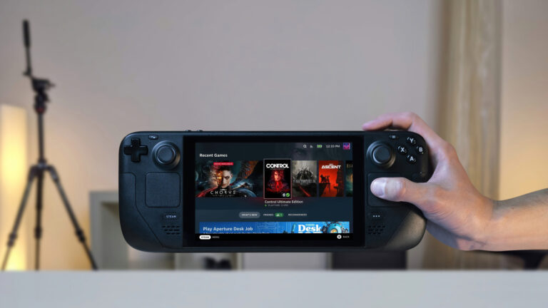 Hand holding a black Steam Deck with its screen powered on.